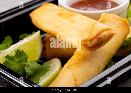 Blick von oben auf asiatische Frühlingsrollen, geschnittene Limette und Chilisauce auf grauem Hintergrund Stockfoto