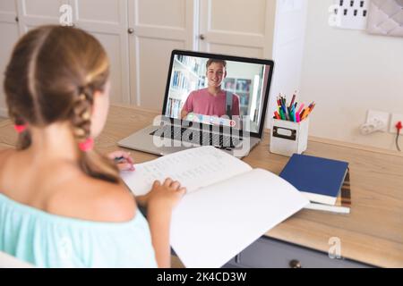 Kaukasisches Mädchen mit Laptop für Videoanruf, mit lächelndem kaukasischen Gymnasiast auf dem Bildschirm. Kommunikationstechnologie und Online-Bildung, digital Stockfoto