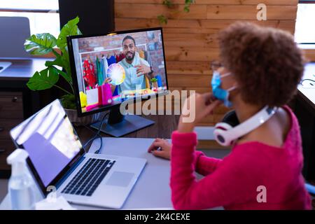 Geschäftsfrau in Gesichtsmaske mit Videoanruf mit Mitarbeiter. Arbeit in einem modernen Büro während covid 19 Coronavirus Pandemie. Stockfoto