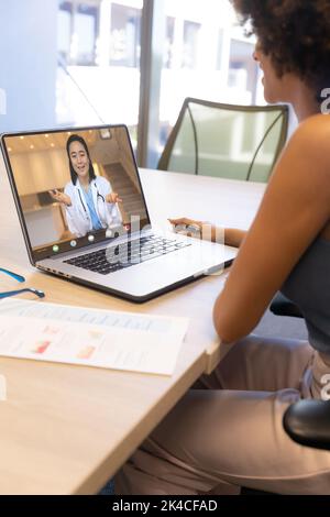 Biracial Frau mit lockigen Haaren im Gespräch mit asiatischen Ärztin auf Videocall über Laptop Stockfoto