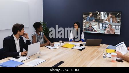 Eine vielfältige Gruppe von Geschäftskollegen, die im Besprechungsraum Videoanruf auf dem Bildschirm haben. Arbeiten Sie in einem modernen Büro. Stockfoto