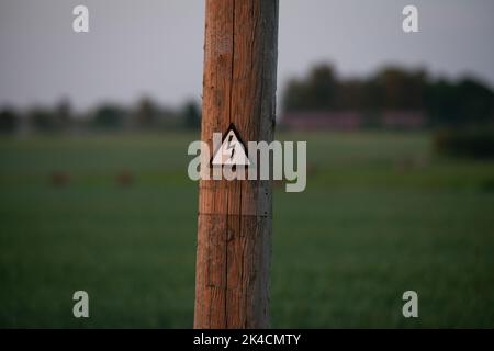 Hochspannungs-Schild auf einem Holzmast. Das Konzept des teuren Stroms. Steigende Energiepreise. Unzugänglicher Strom aufgrund hoher Preise Stockfoto
