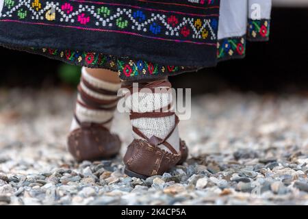 Die Nahaufnahme der Füße eines Kindes mit Ledersandalen und besticktem Rock Stockfoto