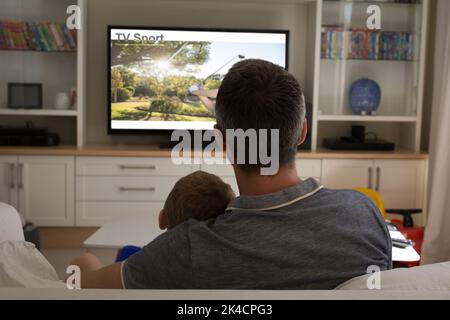 Rückansicht von Vater und Sohn sitzen zu Hause zusammen und beobachten Sportereignis im fernsehen. Sport, Wettbewerb, Unterhaltung und Technologie Konzept digital com Stockfoto