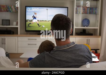 Rückansicht von Vater und Sohn sitzen zu Hause zusammen Fußballspiel im fernsehen. Sport, Wettbewerb, Unterhaltung und Technologie Konzept digital Stockfoto