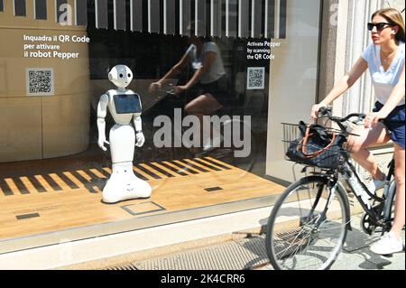 Eine Aufnahme des weißen Pepper-Roboters in einer Bank, um Kunden bei Finanzdienstleistungen zu unterstützen, während eine Frau ein Fahrrad fährt Stockfoto