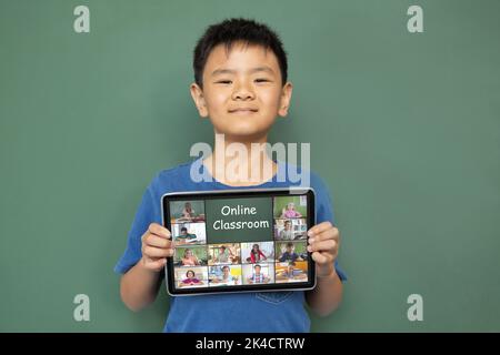 Lächelnder asiatischer Junge hält Tablet für Videoanruf, mit verschiedenen Grundschülern auf dem Bildschirm. Kommunikationstechnik und Online-Bildung, Ziffer Stockfoto