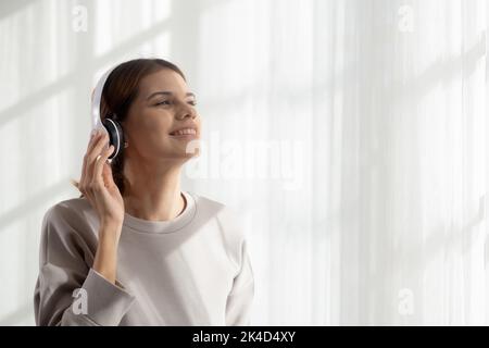 Glückliche junge Frau trägt Kopfhörer Musik hören, während tanzen und singen mit Spaß und genießen Sie im Wohnzimmer, Glück weiblich mit Unterhaltung Stockfoto