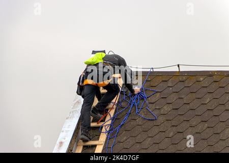 Der Reparaturleiter klettert eine Leiter hoch, während er das Dach repariert Stockfoto