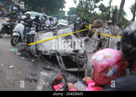 Malang, Indonesien. 1. Oktober 2022. Menschen fahren in der Nähe des Wracks eines verbrannten Autos vor dem Kanjuruhan-Stadion in Malang in der Provinz Ost-Java, Indonesien, 2. Oktober 2022. Mindestens 129 Menschen wurden am Samstagabend bei einem Fußballspiel in der indonesischen Provinz Malang, Ost-Java, getötet und 180 weitere verletzt, wie die indonesische Polizei am Sonntag mitteilte. Quelle: Xinhua/Alamy Live News Stockfoto