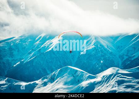 Menschen Paragliding Tandem über dem Berg im Winter in Georgien Skigebiet. Konzept des aktiven Lebensstils und Extremsportabenteuers. Stockfoto