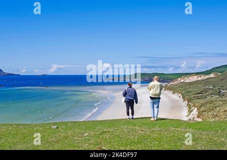 Das junge Paar blickt über den wunderschönen, leeren Strand am Ende der Balnakeil Bay, von Durness, Sutherland, mit einer grasbewachsenen Landzunge von Faraid Head auf der rechten Seite. Stockfoto