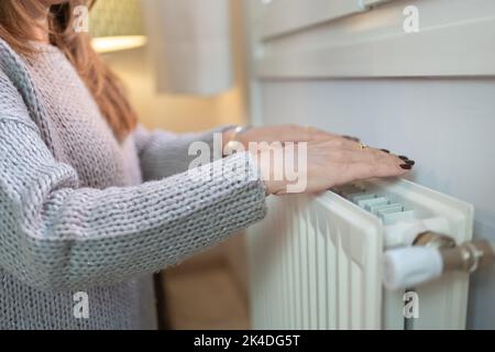 Frau, die sich wegen der Kälte des Winters in einem Heizkörper die Hände wärmte. Stockfoto