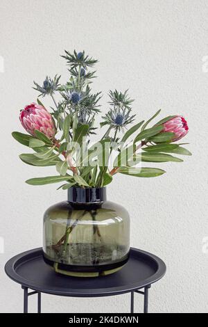 südafrikanische Protea Blume und Eryngium Blumenstrauß in Vase auf dem Tisch Stockfoto