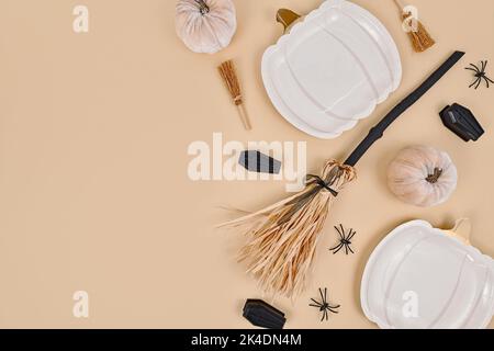 Halloween Party flach lag mit Kürbis geformten Tellern, Hexenbesen, Spinnen und Särgen auf beigem Hintergrund mit Kopierraum Stockfoto