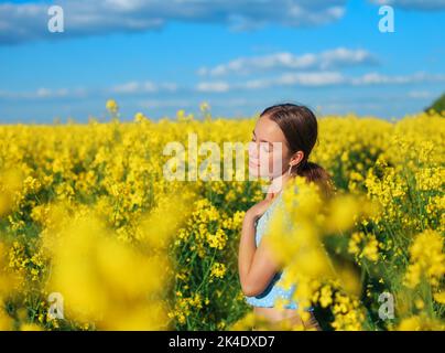 Schöne Teenager-Mädchen lächelt mit gelben Blumen im Sommerfeld Stockfoto