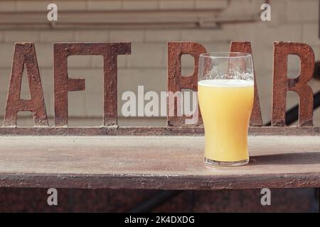 Ein unvollendetes Glas ungefilterten Bieres auf einer Eisentheke. Im Hintergrund ist eine verschwommene façade eines Pubs. Stockfoto