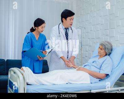 Asiatischer männlicher Arzt, professioneller in weißem Laborkittel, der die Hand eines älteren Patienten zur Kontrolle hält, um den Herzschlagpuls zu untersuchen, und ein Pflegeassistent, der nicht nimmt Stockfoto