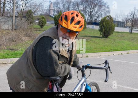 Schönes Außenportrait eines bärtigen, kaukasischen ukrainischen Senioren, der auf der Suche ist, wenn er sich bereit macht, auf einem Schotterfahrrad zu fahren Stockfoto