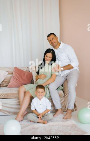 Die Schwangerin sitzt auf einem Sofa, umgeben von ihrem Mann und ihrem Sohn Stockfoto
