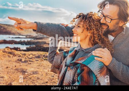 Ein Paar genießt die Freizeitaktivitäten im Freien mit Freude. Mann umarmt Frau aus Beck und Zeigefinger, um ihre schöne Landschaft zu zeigen. Menschen im Urlaub Stockfoto