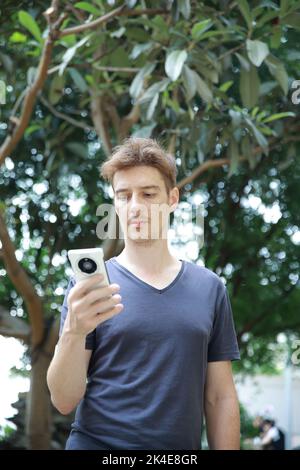 Rothaariger europäischer Mann mit Sommersprossen, der mit seinem Mobiltelefon spielt Stockfoto