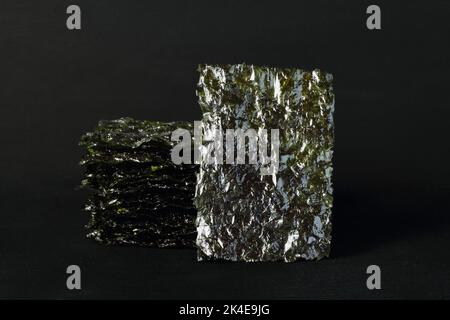 Gewürzter Seetang-Snack. Algenblätter in einem Stapel auf schwarzem Hintergrund gestapelt. Stockfoto