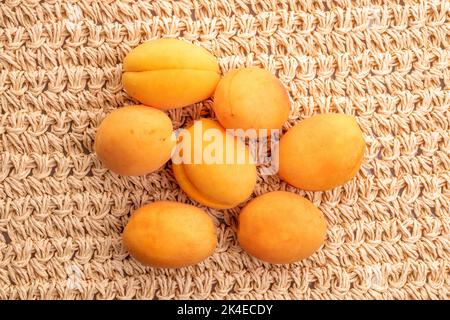 Mehrere Bio-gelbe Ananas-Aprikosen, Makro, auf einer Strohmatte, Draufsicht. Stockfoto