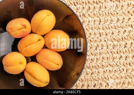 Mehrere reife gelbe Ananas-Aprikosen auf einem schwarzen Teller, Nahaufnahme, auf einer Strohmatte, Draufsicht. Stockfoto