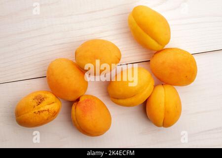 Mehrere Bio-gelbe Ananas-Aprikosen, Nahaufnahme, auf einem weißen Holztisch, Draufsicht. Stockfoto