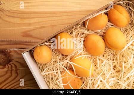 Mehrere reife gelbe Ananas-Aprikosen in einer Schachtel mit Holzschnitzeln, Nahaufnahme, auf einem Holztisch, Draufsicht. Stockfoto