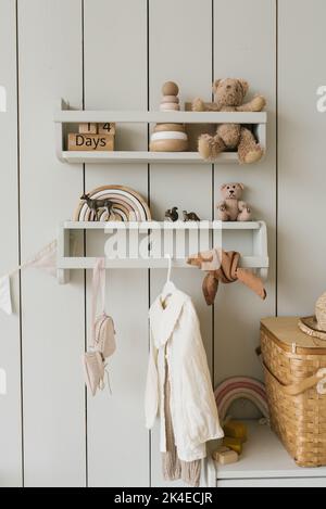 An einem Kleiderbügel im Kinderzimmer hängen Kinderkleidung und verschiedene Spielzeuge im minimalistischen Stil Stockfoto