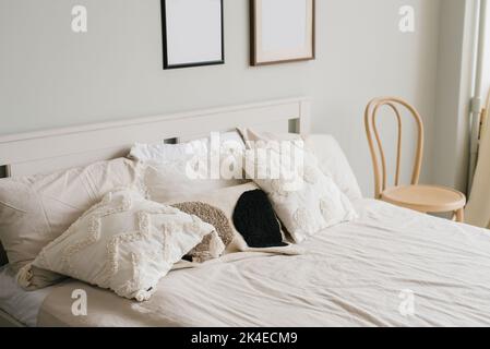 Bett im Schlafzimmer in einem skandinavischen minimalistischen Stil. Leichte Kissen auf dem Bett. Einrichtung über dem Bettrahmen Stockfoto