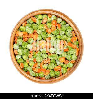 Dehydrierte grüne Erbsen und Karottenstücke in einer Holzschüssel. Gemischtes Gemüse. Samen der Hülse Frucht Pisum sativum, und schneiden Sie orange Karotten, Daucus carota. Stockfoto