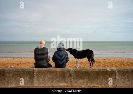 Paar sitzen am Strand mit Hund in Portobello, Edinburgh, Schottland, Großbritannien Stockfoto