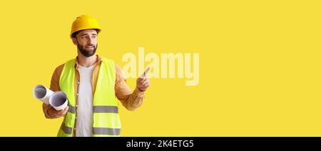 Builder mit Zeichnungen, die auf etwas auf gelbem Hintergrund mit Platz für Text zeigen Stockfoto
