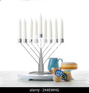 Menorah mit Kerzen, Dreidellen und Donut für die Chanukka-Feier auf hellem Holztisch vor weißem Hintergrund Stockfoto