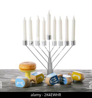 Menorah mit Kerzen, Donut und Dreidels für die Chanukka-Feier auf einem grauen Holztisch vor weißem Hintergrund Stockfoto