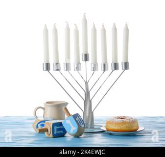 Menorah mit Kerzen, Dreidellen und Donut für Chanukka-Feier auf farbigem Holztisch vor weißem Hintergrund Stockfoto