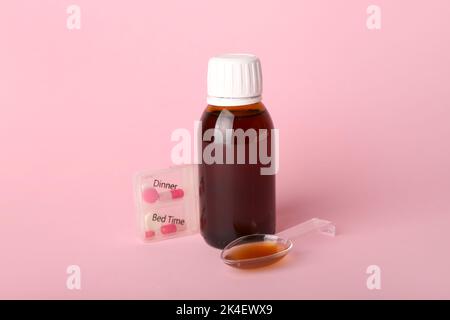 Flasche Hustensirup, Löffel und Pillen auf rosa Hintergrund Stockfoto