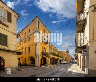 Fossano, Piemont, Italien - 09. September 2022: Blick auf die gepflasterte Straße Via Roma mit antiken Gebäuden und Arkaden und dem Bürgerturm im Hintergrund Stockfoto