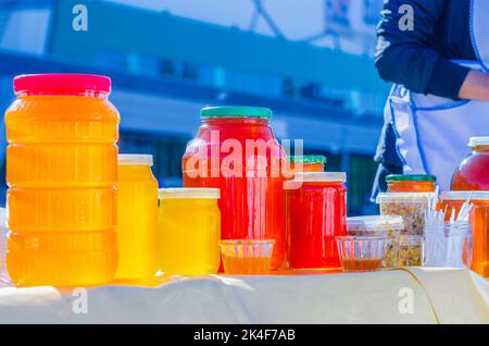 Landwirtschaftliches Produkt zum Verkauf vorbereitet. Auf der Theke befinden sich verschiedene Gläser und Behälter, die mit buntem Bashkir-Honig gefüllt sind. Herbstmarkt. Stockfoto