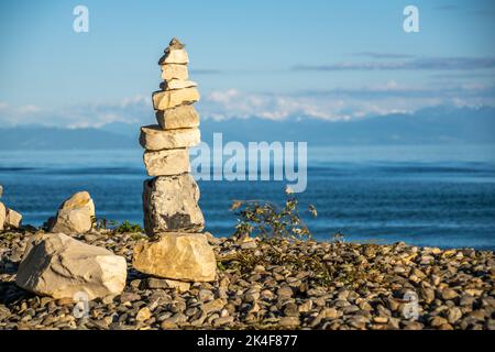 Steinpyramiden am Seeufer mit Blick auf die Berge und sonnigen blauen Himmel Stockfoto