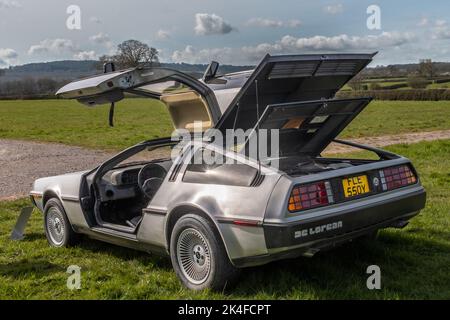 Eine 3/4-Heckansicht eines DeLorean DMC12 aus dem Jahr 1983, der auf Gras geparkt ist, wobei sowohl die Flügeltüren als auch die hintere Motorabdeckung offen sind, um bei einem Treffen von Oldtimer zu sehen Stockfoto