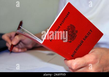 Das Mädchen hält einen von der Russischen Föderation ausgestellten Militärausweis in der Hand und schreibt seine Daten auf. Übersetzung: 'Russische Föderation', 'Militärausweis' Stockfoto