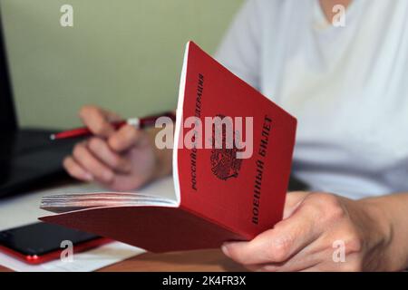 Das Mädchen hält einen von der Russischen Föderation ausgestellten Militärausweis in der Hand und schreibt seine Daten auf. Übersetzung: 'Russische Föderation', 'Militärausweis' Stockfoto