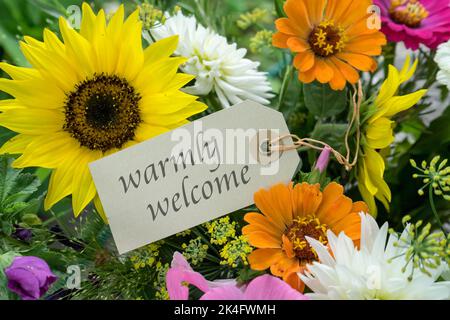 Farbenfroher Blumenstrauß mit Karte und englischem Text: Herzlich willkommen Stockfoto