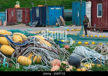 Lagunnoe, Russland - 01. August 2022: Fischer überprüft und repariert industrielle Fischernetze am Ufer eines Fischereistützpunkes Stockfoto