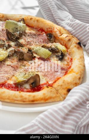 Pizza capricciosa mit weißen Pilzen, Schinken, Artischocke, Tomaten, Oliven, parmesan und Mozzarella auf weißem Hintergrund für Restaurantmenü.Nahaufnahme Stockfoto