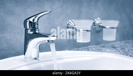 Wassermischer im Bad. Wasserhahn aus Chrom-Material, Wasserhahn mit Wasser in Blauton Stockfoto